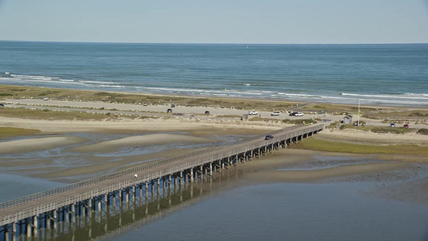 A long bridge over a body of water leading to a strip of coastal land with a beach