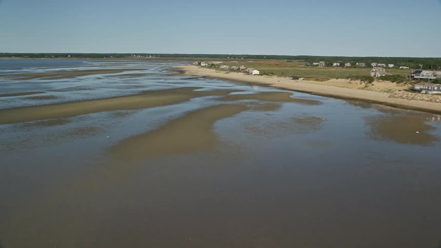A boat sails in the water with sand bars along the beach at low tide near a coastal town