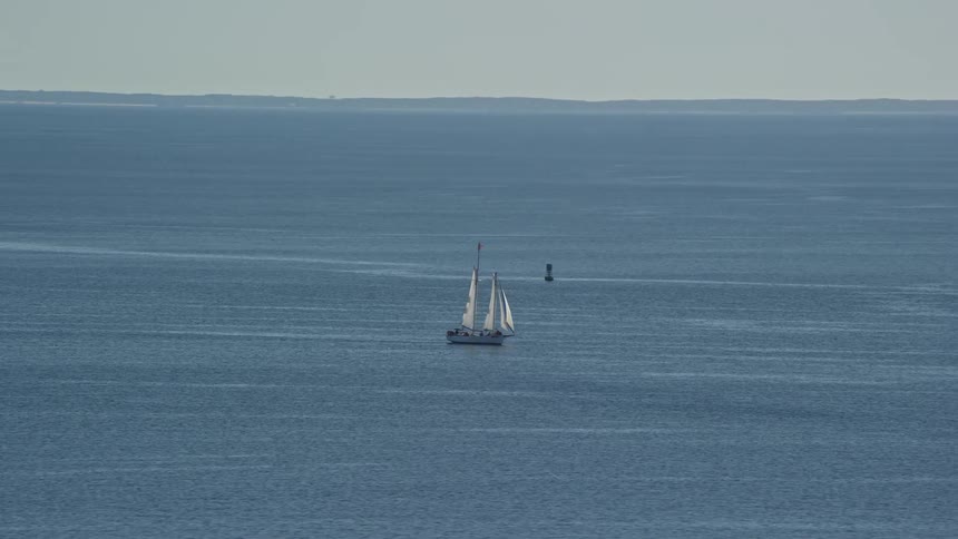 Sailboat sails past buoy floating far from the coast