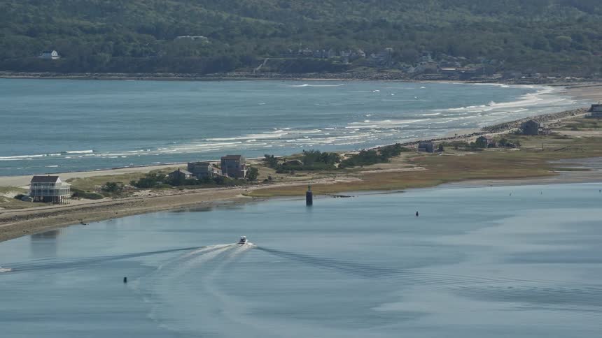 Motorboat moves through lagoon opposite ocean near coastal town