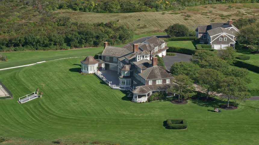Truck carries large plant across lawn of coastal mansion near undeveloped fields