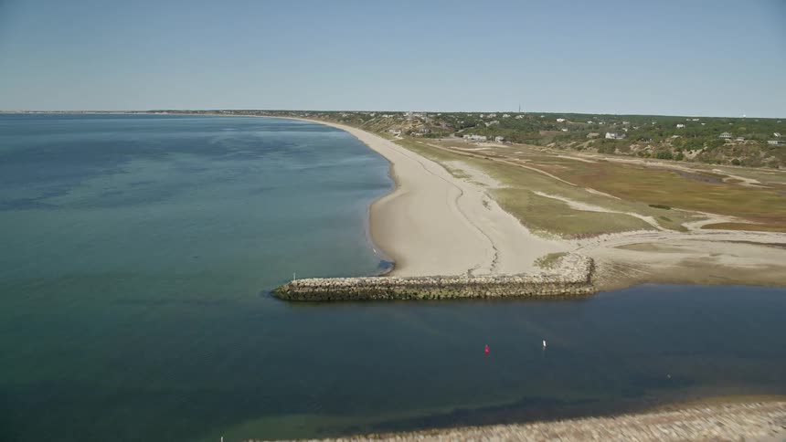Coastal town borders beach a fields width from river mouth on a sunny day