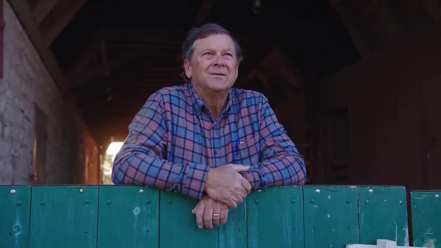 Man leaning against a fence next to a stable