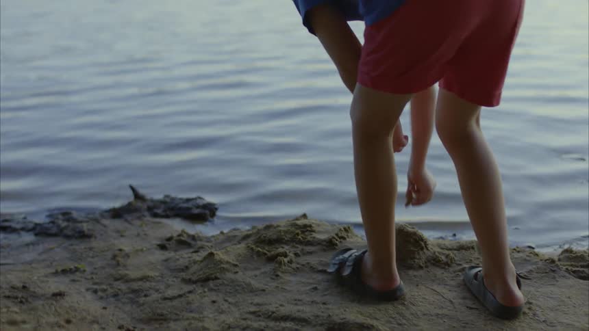 A boy walks to the shoreline and picks up a rock to skip