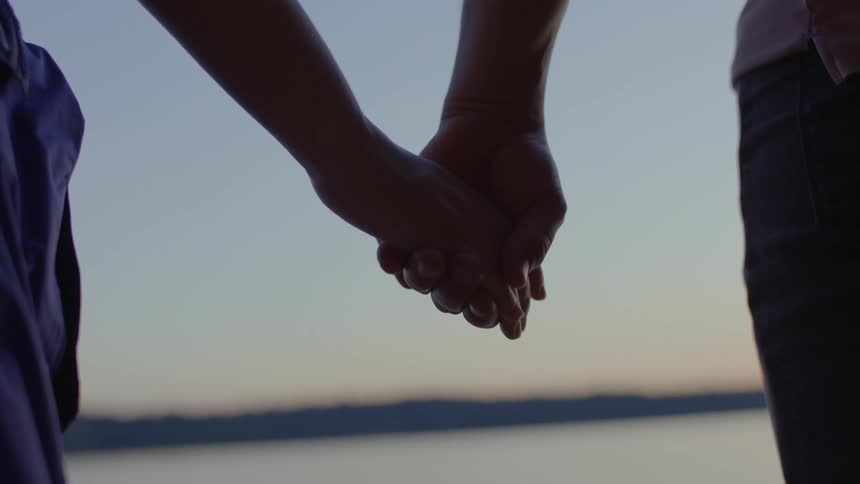 Closeup of holding hands lakeside at sunset