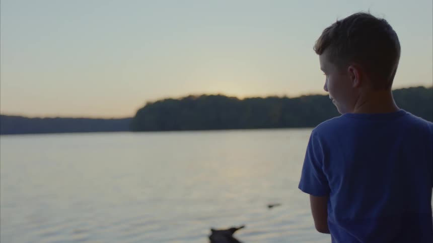 Boy skips stones at the lake during sunset