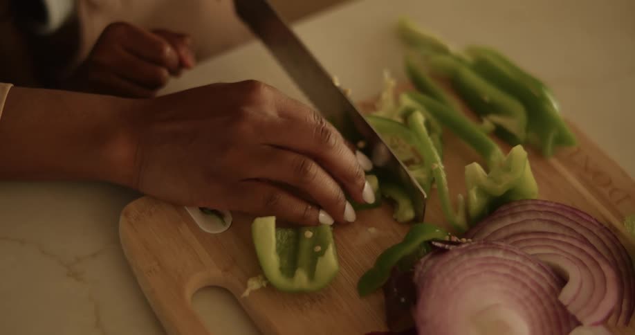 A woman holds green peppers and slices them on a cutting board