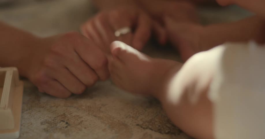 An adult hand is shaking a babys foot as they sit on the floor and play