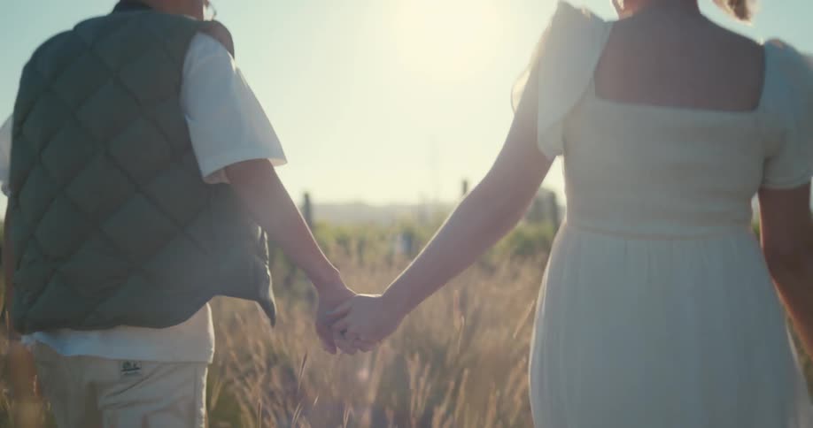 A couple holding hands while walking through a field of tall grass