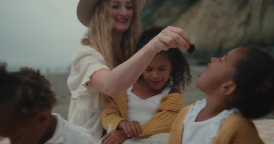 Three children and two adults having a picnic outdoors and the woman gives a cookie to one of the children
