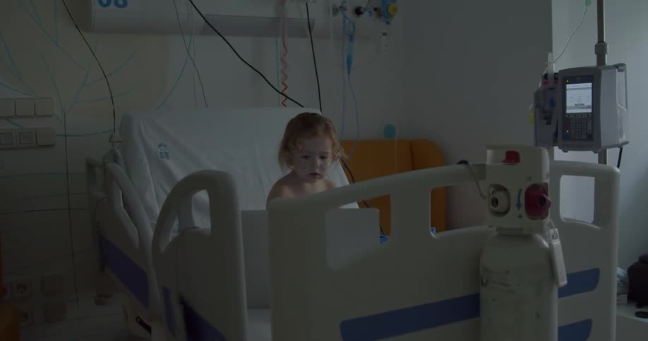 Little blonde girl sits on a bed in the hospital