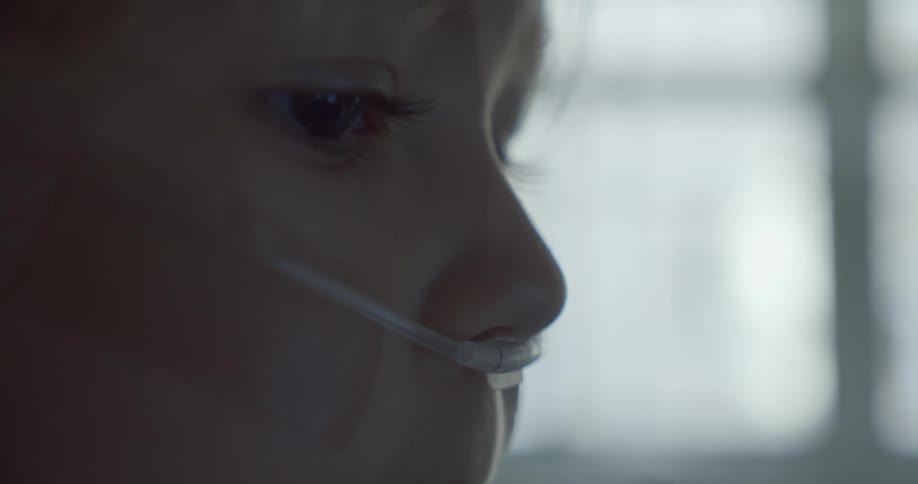 A young child in the hospital has an oxygen tube across her face and a nasal cannula in her nose and tape on her cheek