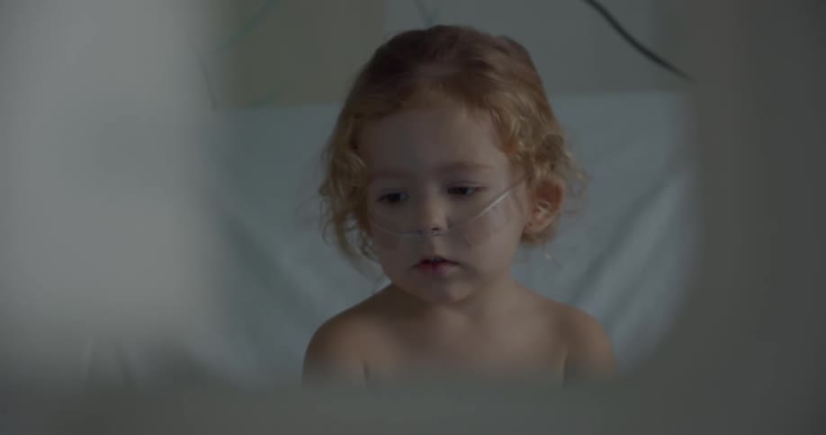 Child sitting on a hospital bed with nursing tubes on their face