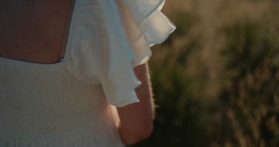 Back view of lady in a white dress standing near some grasses at midday