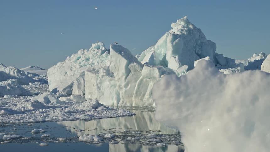 Several icebergs of white ice on top of the water and birds flying in the sky
