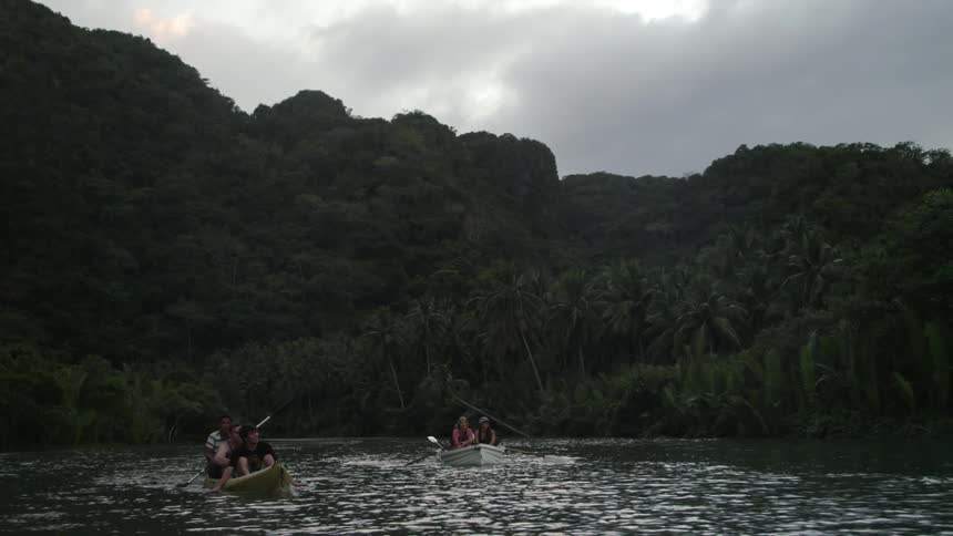 People in two row boats going down a body of water on a cloudy day