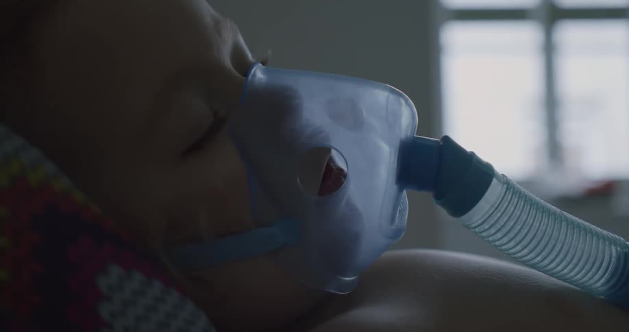 A child sleeping on a hospital bed with medical equipment on their face