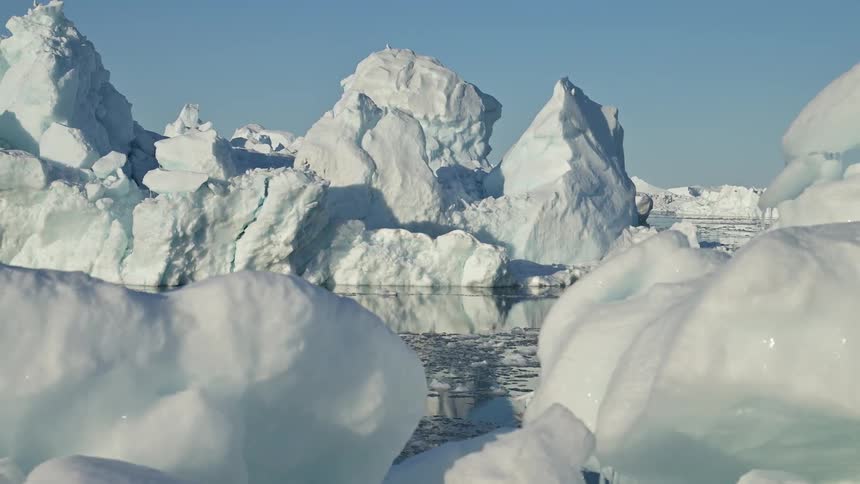 Iceberg slowly floats through reflective sea near ice covered shore