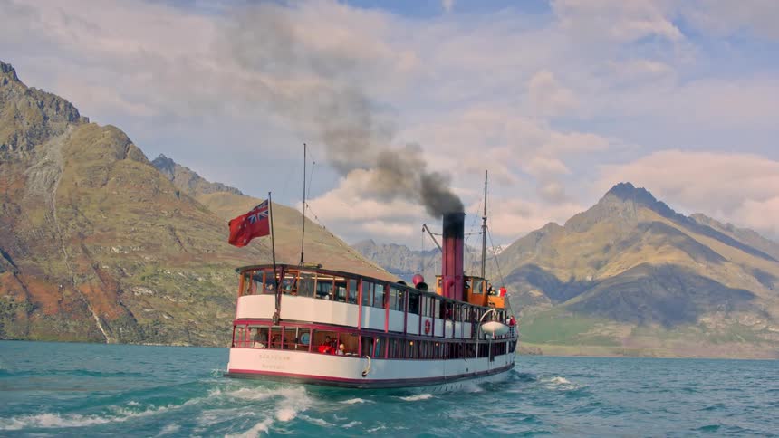 An iconic Queenstown steamship boat crossing a lake towards a mountain range in New Zealand