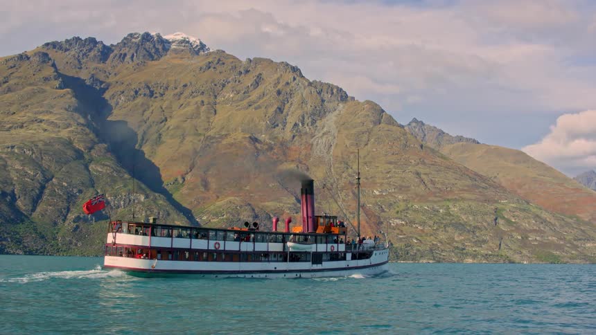 A beautiful historic steamship is traveling past the mountain