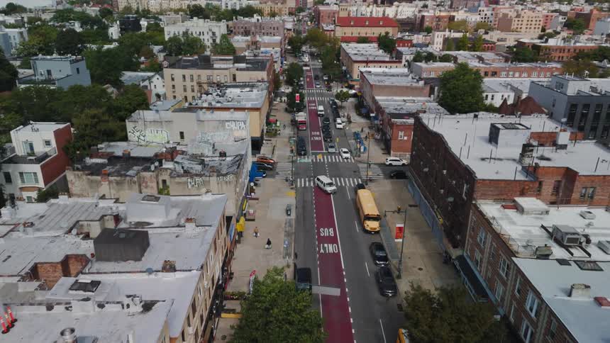 A large street in a residential area with a few cars stopped at traffic lights