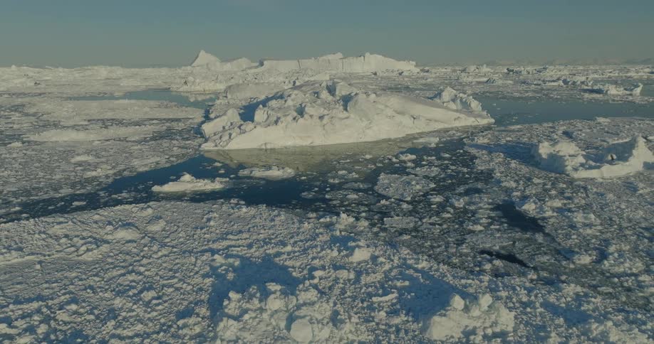The sun shines upon broken pieces of melting ice floating in the arctic water