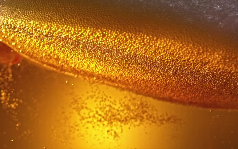 Light shines upon small bubbles as they float to the top and move in a golden brown liquid