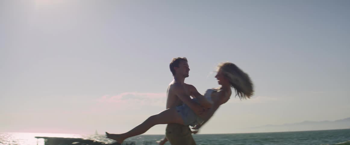 A shirtless man and a woman having fun by the beach at sunset