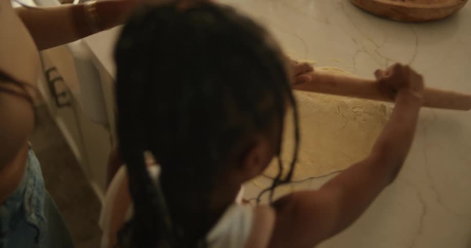 A little girl using a pinch roller to knead dough on the table