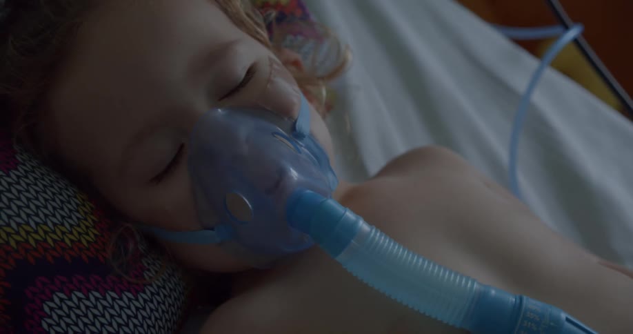 A child lying asleep on a hospital bed with medical equipment on their face