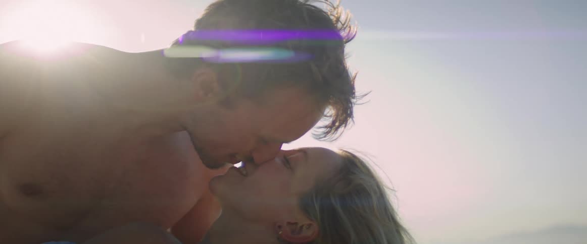A shirtless man and a woman kissing at midday