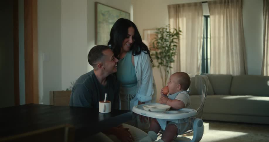 A couple cares for their baby while a woman kisses their forehead both of them laughing