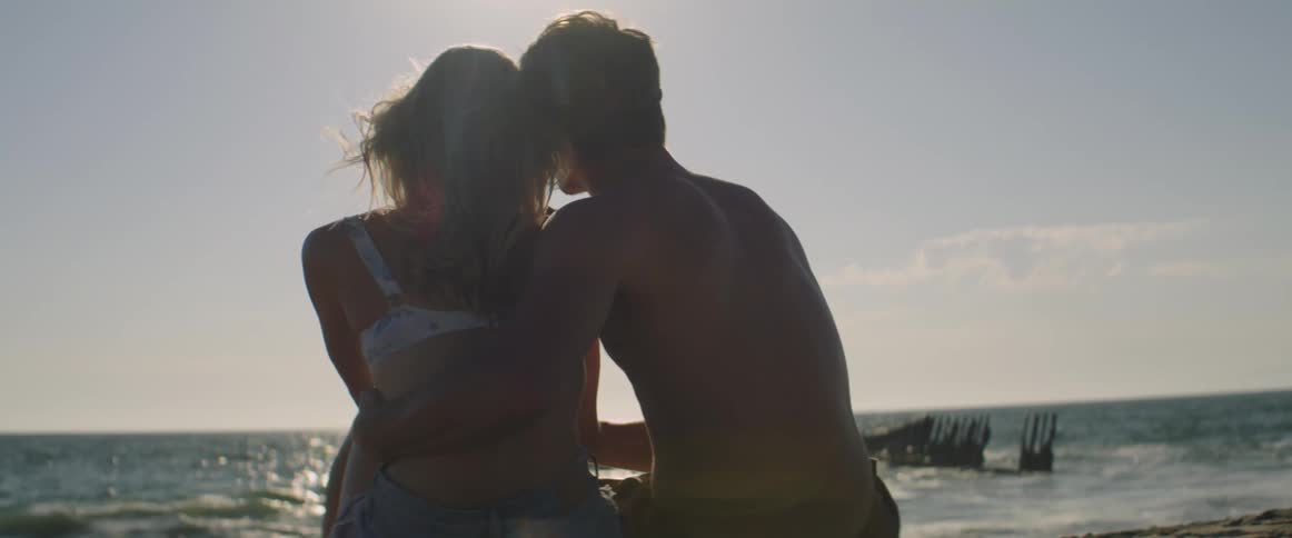 A man and a woman romancing while sitting by the beach