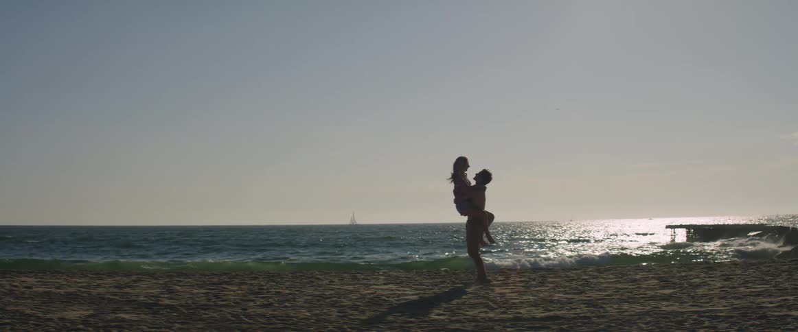 On a beach a woman runs towards a man and jumps into his arms