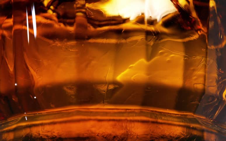 Ice cube melting on an amber liquor inside a glass