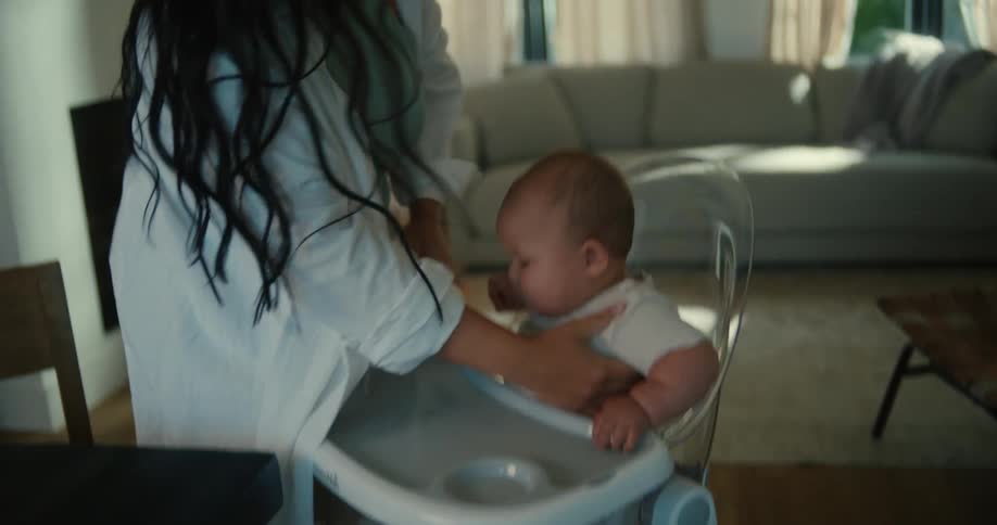 A mother placing her child in a high chair while the spouse fastens a bib onto the child getting ready to start eating