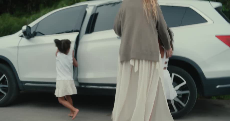 White woman crossing a road with two black girls and running towards a white car before opening the doors and entering the vehicle