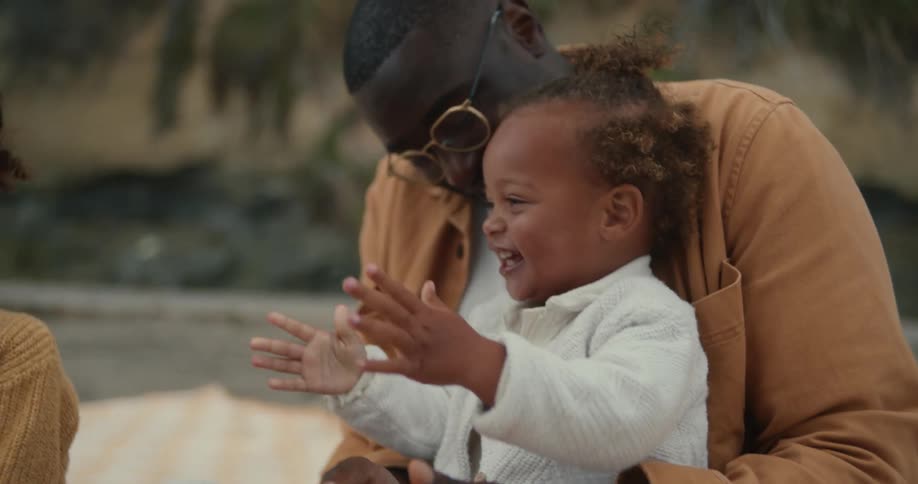 A man on a beach playing with the infant girl in his lap