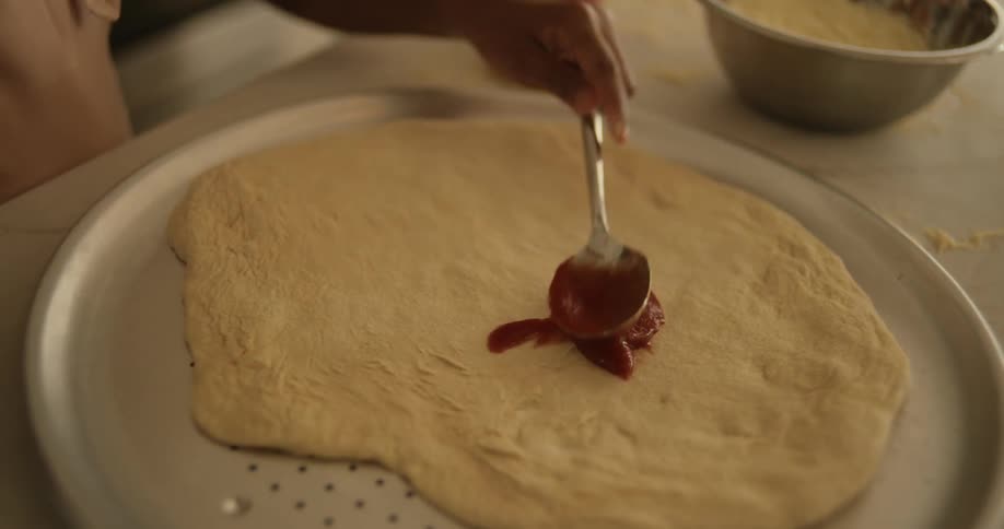 A little girl scooping sauce with a spoon and pouring it into some pasta on the table
