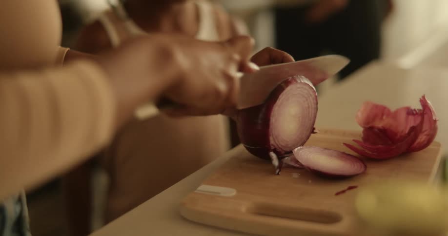 Black woman slicing a red onion on top of a cutting board while a black girl smiles and talks around her
