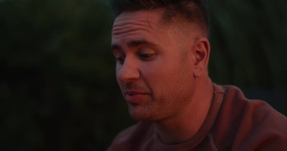 Man in green sweater talks to people near a fire pit in the yard