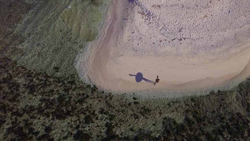 A person is holding a surfboard on the small deserted island