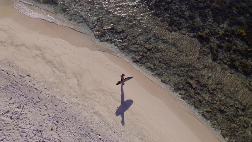 A surfer standing on the sea shore looking forward with the board in his arms