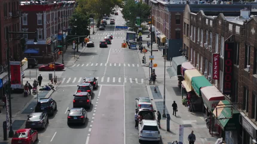 A street with a few cars in a residential area with people walking on the sidewalks