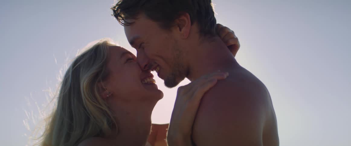 Shirtless man and woman kissing at sunset