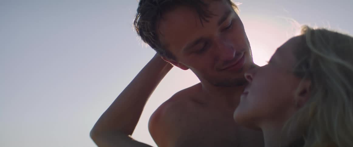 A blonde woman gazes into a mans eyes while gently caressing the back of his head