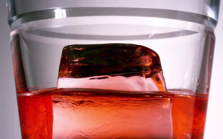Closeup of a glass with a shot of a drink and a spinning ice cube