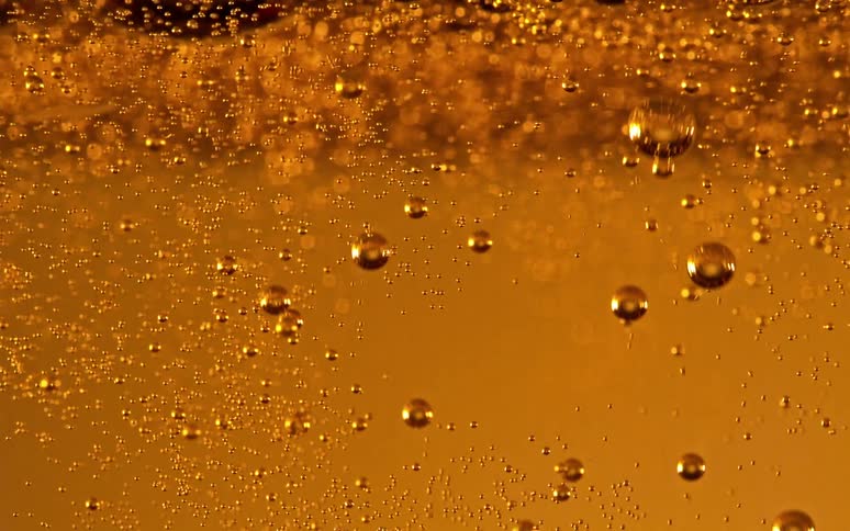Bubbles float and sway as they rise to the surface in a golden brown liquid