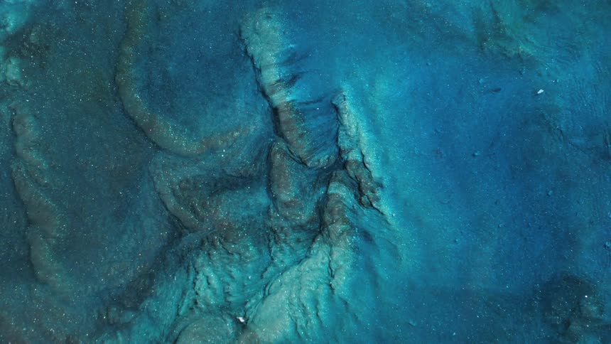 Light shines on sparkling glitter as it flows over a blue textured surface