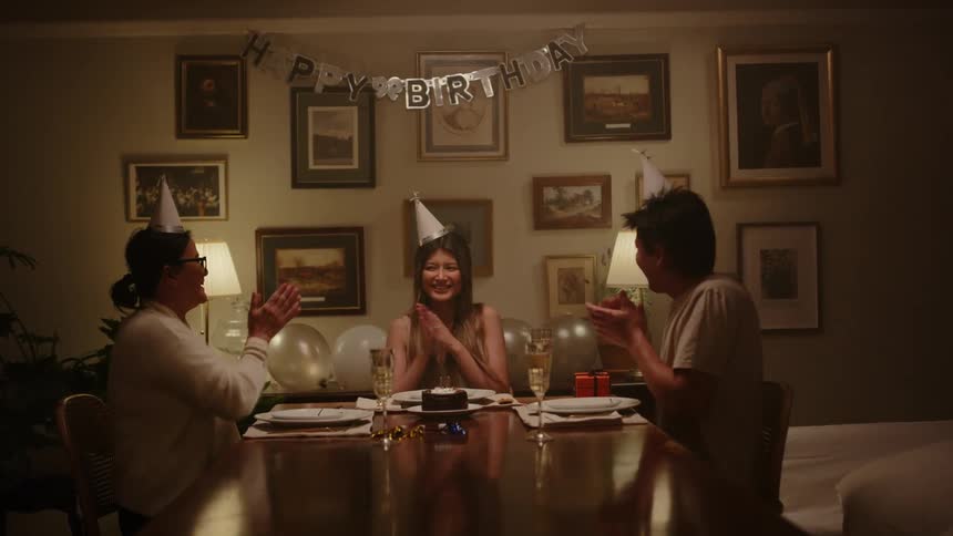 Sitting at a long table the mother and father clap as their daughter blows out the candles